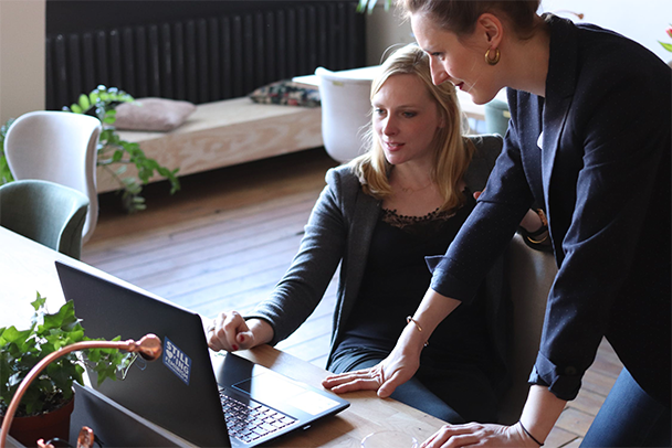Two women are engaged in a discussion while working on a laptop