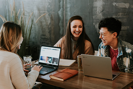 Three people engaged in a conversation, laughing while working on their laptops