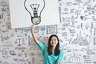 a woman smiling while holding up a board with a light bulb illustration, symbolizing creativity and new ideas